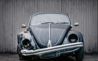 Front facing shot of a old fashioned grey car with half of its front damaged.